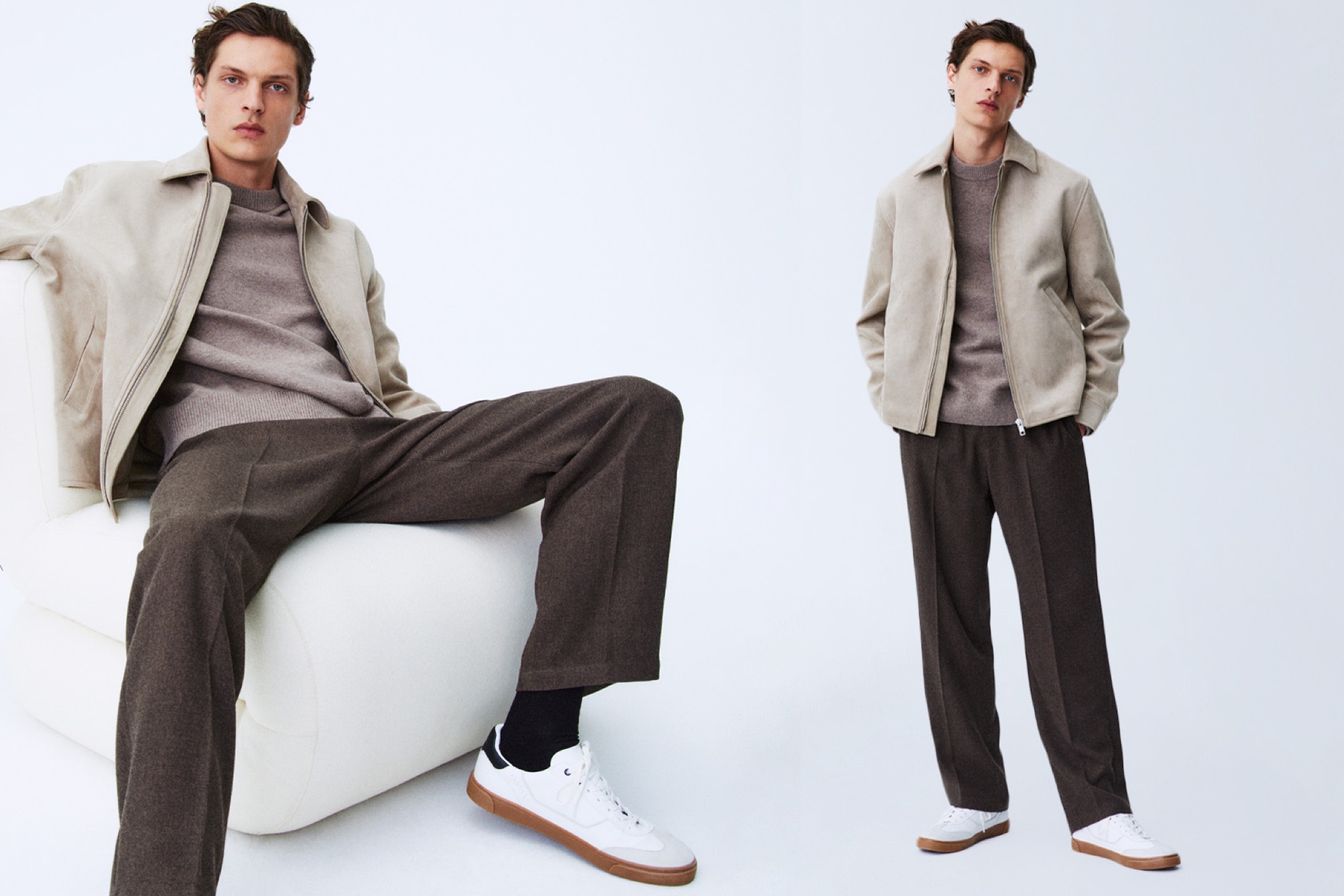 Hombre con cazadora en blanco roto, jersey de punto fino en beige y pantalones poco ajustados en marrón oscuro con deportivas blancas.